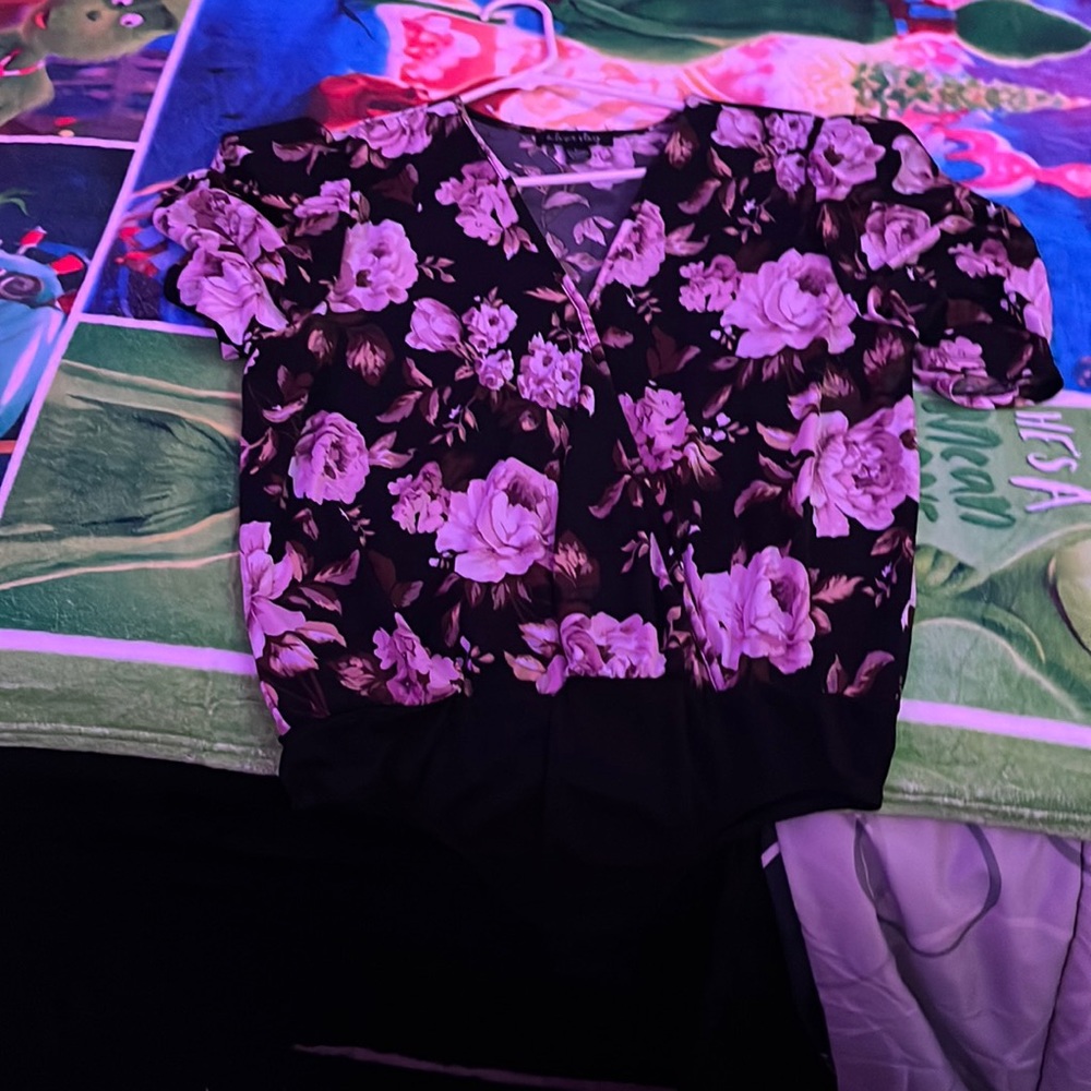 This is a beautiful black button up body suit with a light pink floral design .
